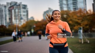 Young happy athletic woman listening music on earphones while jogging in the park.